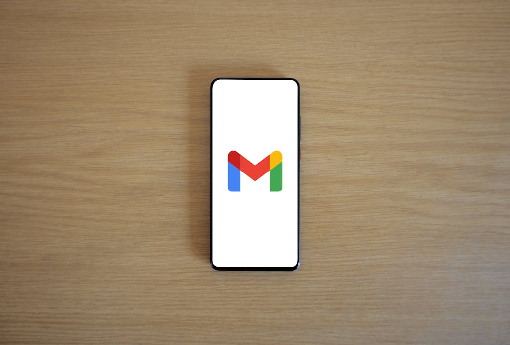 A smartphone displaying the Gmail app logo on a wooden surface, viewed from above.